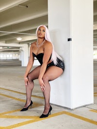 a woman in black stockings leaning against a wall in a parking lot